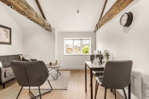 A modern living room with a sofa, chairs, a dining table, and a window with a city view. - Bright 1BR Modern Apartment in Sheffield Centre (Sheffield)