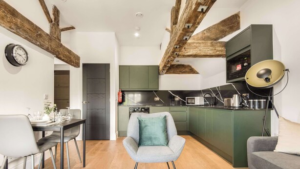 Una cucina moderna con mobili verdi, una zona pranzo con tavolo e sedie, e travi a vista in legno al soffitto.