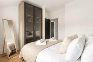A bedroom with a bed, a wardrobe, a mirror, and a door leading to another room. - Bright 1BR Modern Apartment in Sheffield Centre (Sheffield)