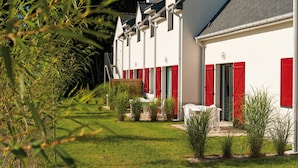 A row of white buildings with red shutters, a grassy lawn, and a clear sky. - Morbihan Golf Apartment for 4 (Queven)