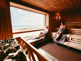 Una sauna con bancos de madera y un amplio ventanal con vista a la playa.