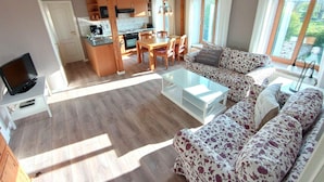 Un amplio salón con sofá, mesa de centro y televisor. Se observa una cocina con armarios de madera y un comedor con sillas.