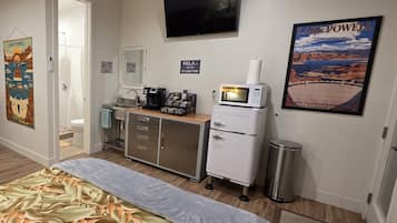 Una camera d'albergo con un letto, angolo cottura, televisione e un poster del Lago Powell, oltre a un ingresso che conduce al bagno.