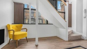 Une pièce avec une chaise jaune, un escalier et une vue sur les bâtiments à l’extérieur.
