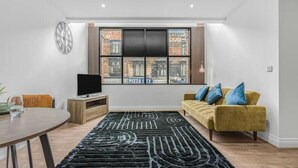 Un salon moderne avec un canapé, un téléviseur à écran plat, une table à manger et un tapis à motifs.