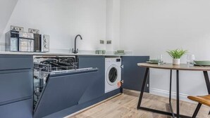 Une cuisine compacte équipée d’un lave-vaisselle, d’un lave-linge et d’un petit coin repas avec une table et des chaises.