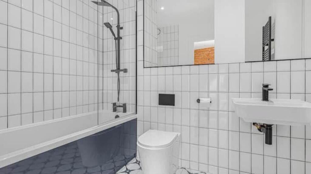 A modern bathroom with white tiled walls, a bathtub, a toilet, and a sink.