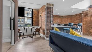Ein modernes Interieur mit Backsteinwand, Essbereich mit Stühlen, einer Couch und Blick auf ein Gebäude.