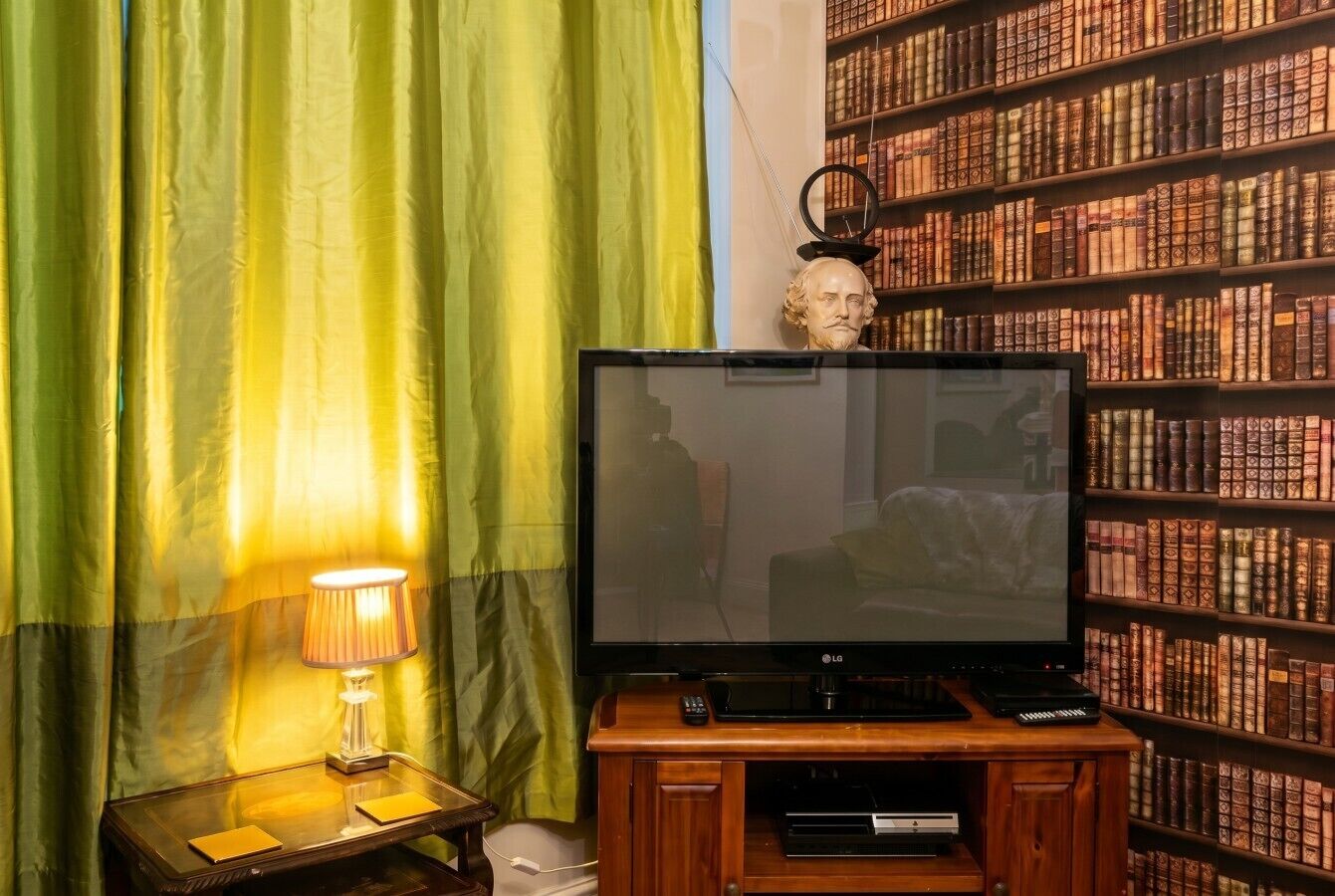A room with a television on a wooden stand, a lamp on a side table, and a bookshelf filled with books.