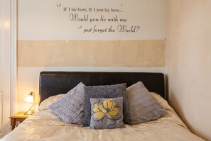 A neatly made bed with a headboard, a bedside lamp, and a wall with a quote.