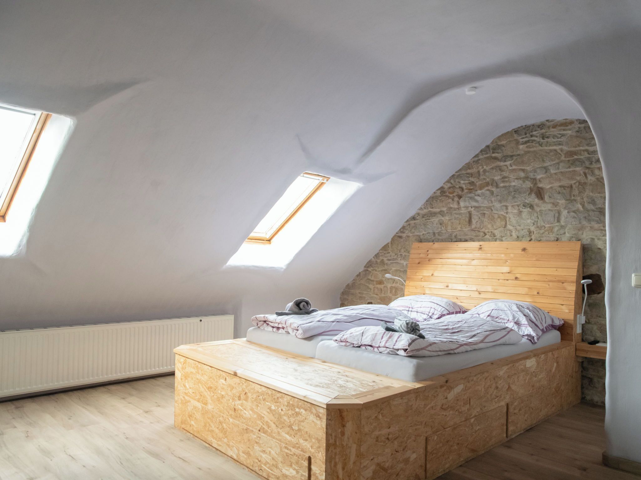 A loft bedroom with a sloped ceiling, wooden headboard, and a built-in bed.