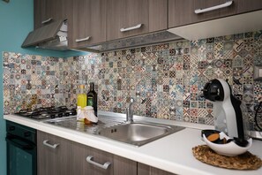 A kitchen with a patterned tile backsplash, a stainless steel sink, and a coffee maker on the counter. - SUITE 35 apartment 200 mt from the sea and 20 minutes from Tropea (Santa Maria)
