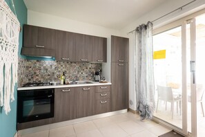 Une cuisine avec des meubles de couleur bois foncé, un pare-feu décoré, une cuisinière à gaz et une porte-fenêtre coulissante donnant sur un espace extérieur.