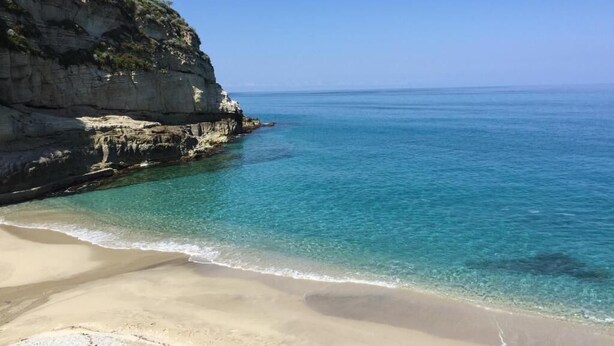 Een strand met helder turquoise water, een zandstrand en rotsachtige kliffen.