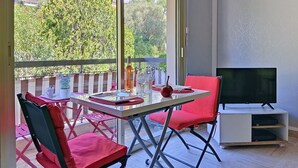 Un balcón con una mesa lista para comer, un televisor y una silla roja.