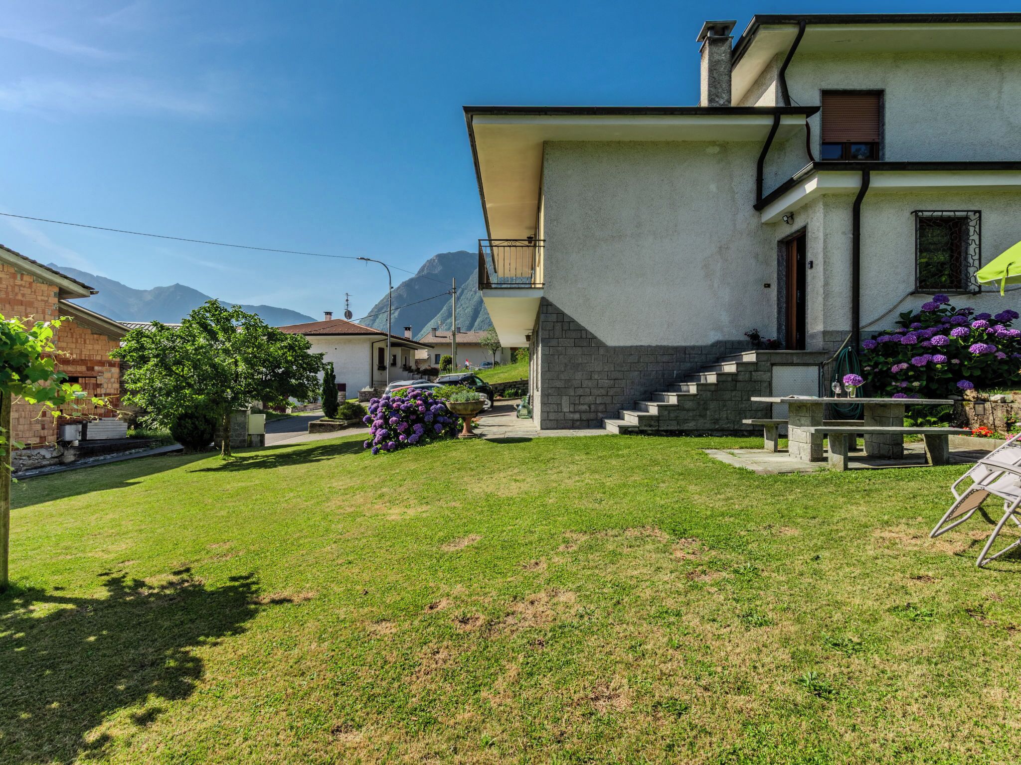 Un edificio residenziale con un cortile anteriore, una scalinata che conduce all'ingresso e vista sulle montagne sullo sfondo.