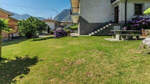Un edificio residencial con un jardín delantero, una escalera que lleva a la entrada y vistas de montañas al fondo.