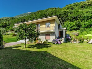 Ein zweistöckiges Haus mit Balkon, umgeben von einem gepflegten Rasen und blühenden Pflanzen.