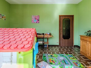 Ein Zimmer mit Spielbereich, einer Holztür und einem gemusterten Boden.