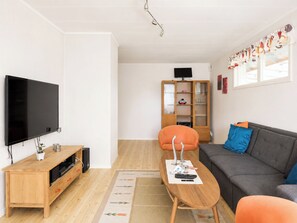 En stue med et fladskærms-TV, træmøbler, en grå sofa og et skab.
