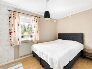 Een slaapkamer met een bed, gordijnen, een raam, een radiator en een hanglamp.