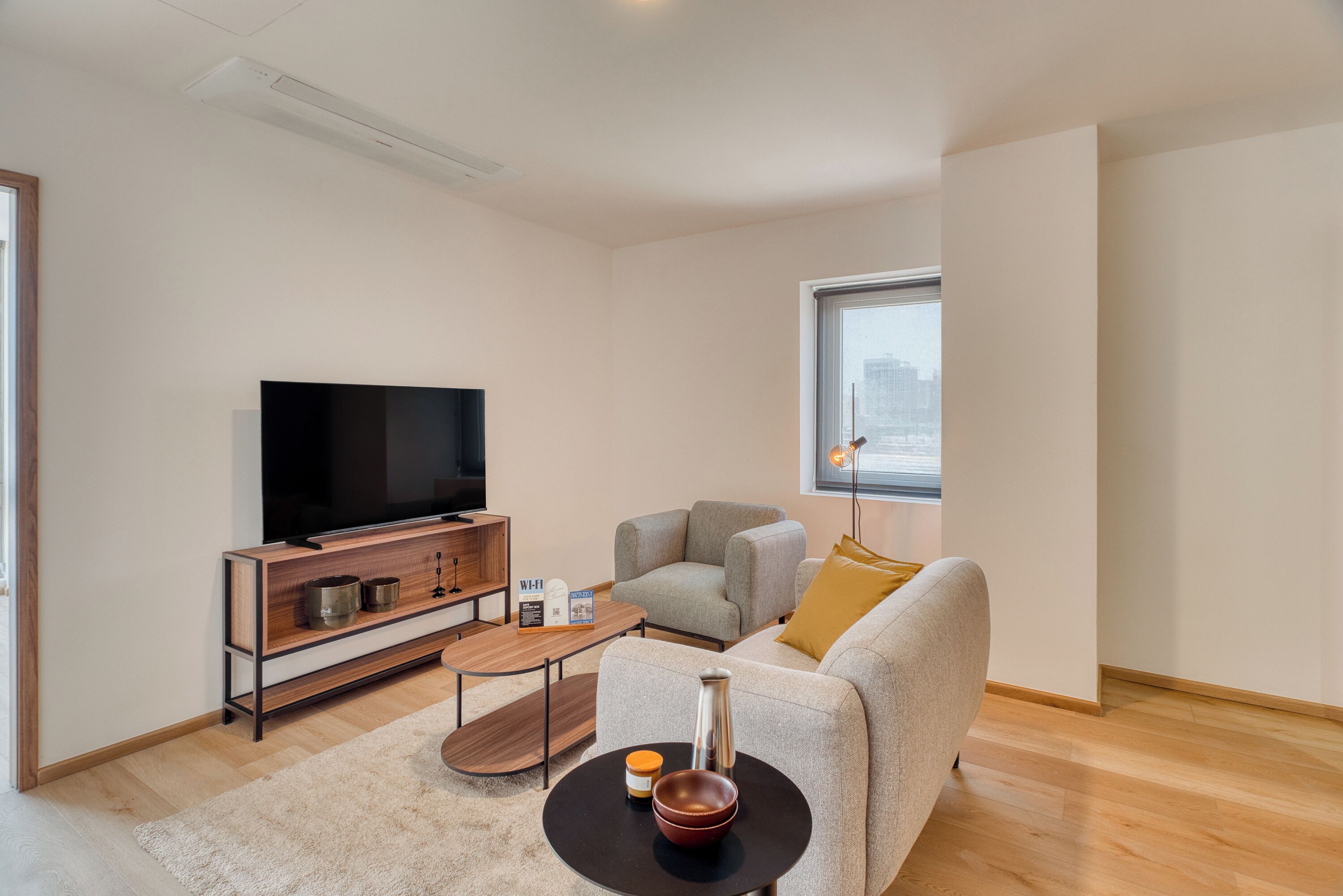 Una sala moderna con una televisión de pantalla plana, un sofá, una mesa de centro y vistas de la ciudad a través de un ventanal grande.