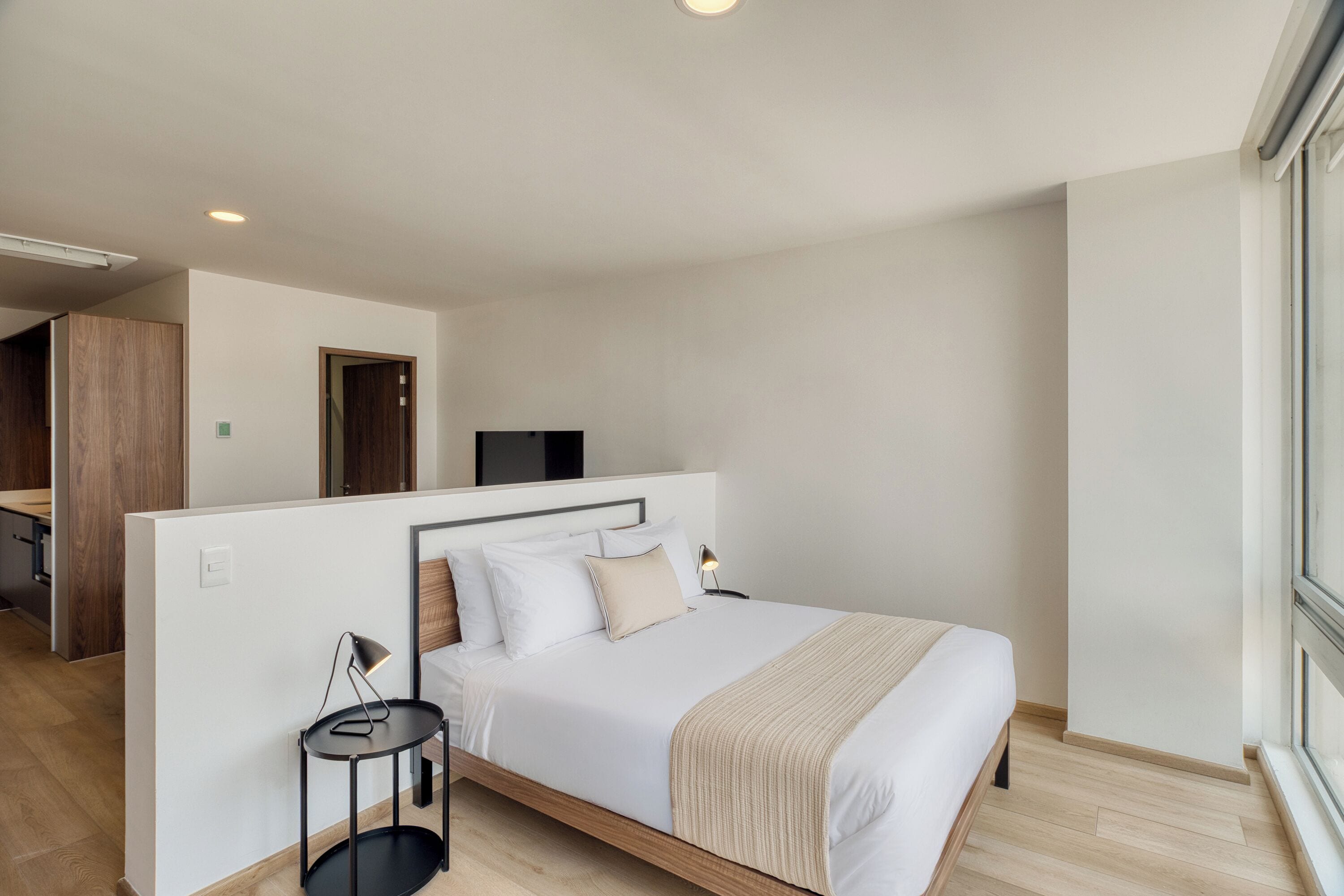 A modern hotel room with a bed, bedside table, lamp, and a TV.