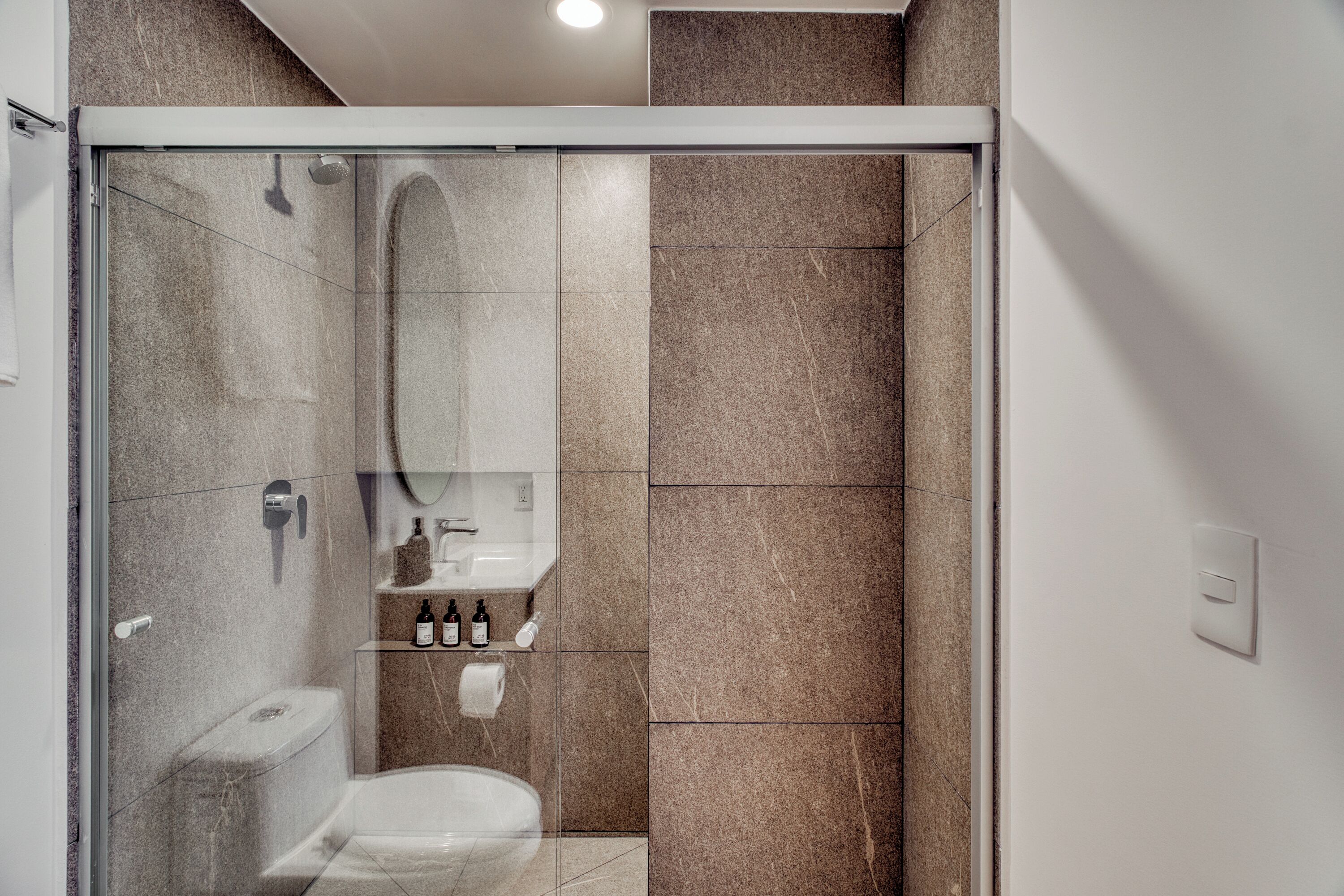 A modern bathroom with a glass shower enclosure, a toilet, a sink with toiletries, and a mirror.