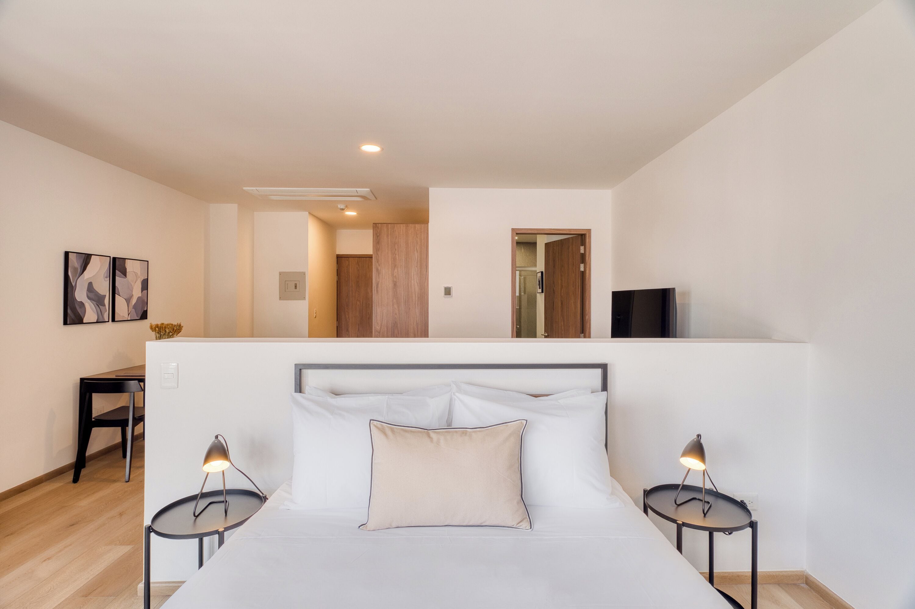 Un dormitorio con una cama, dos mesitas de noche, un televisor y una puerta que da a otra habitación.