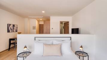 Un dormitorio con una cama, dos mesitas de noche, un televisor y una puerta que da a otra habitación.