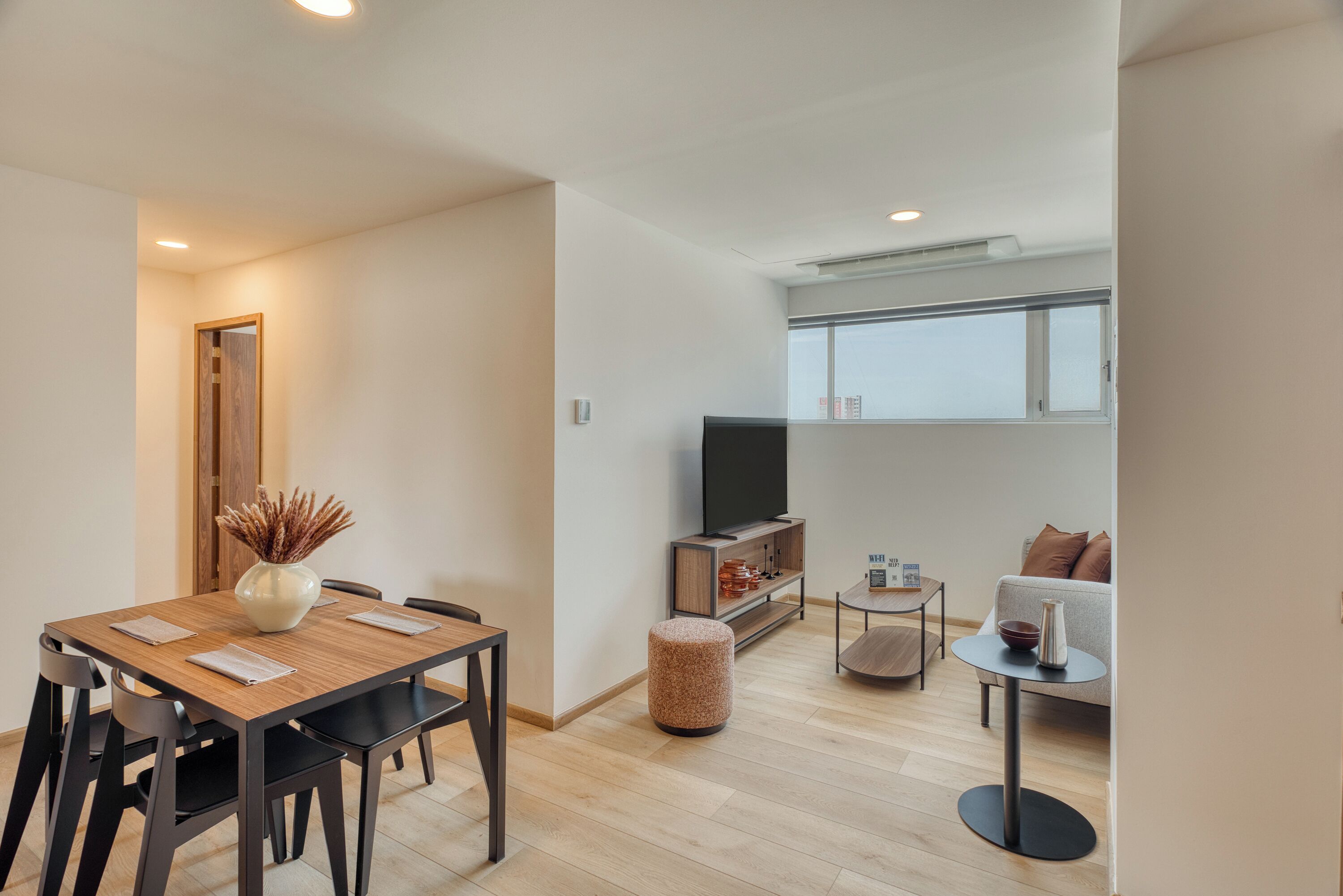 A modern living space with a dining area, a sofa, a TV, and a window.