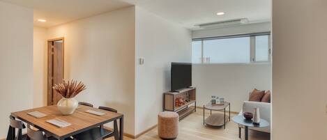A modern living space with a dining area, a sofa, a TV, and a window.