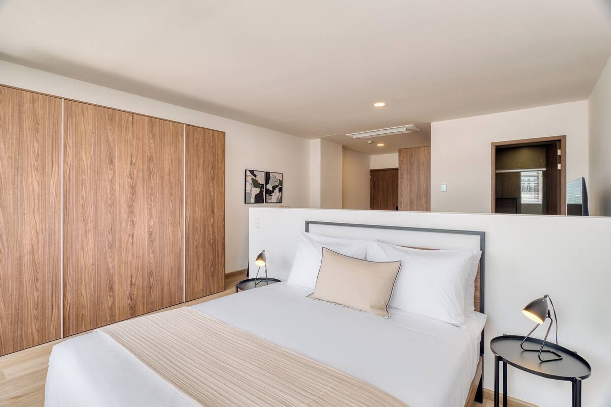 Un dormitorio moderno con una cama grande, un armario de madera, mesitas de noche y un espejo.