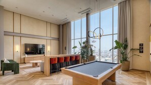 Ein moderner Raum mit Billardtisch, Bar, Sitzgelegenheiten und großen Fenstern.