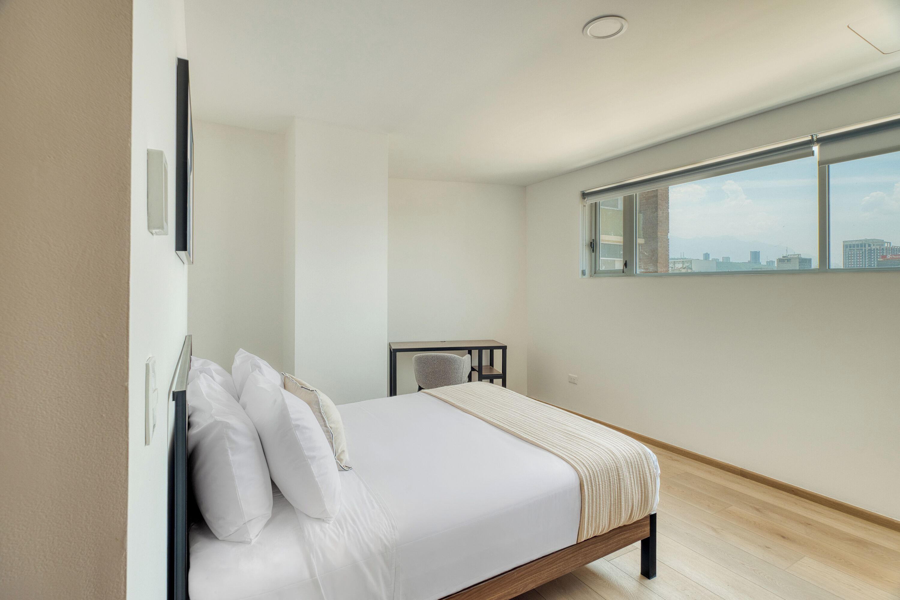 A modern bedroom with a bed, a desk, and a window with a city view.