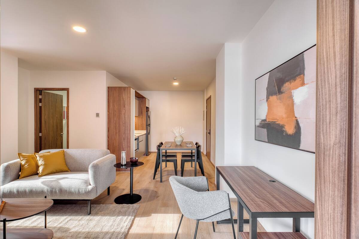 Una sala moderna con sofá, sillón, mesa de comedor y una obra de arte en la pared.