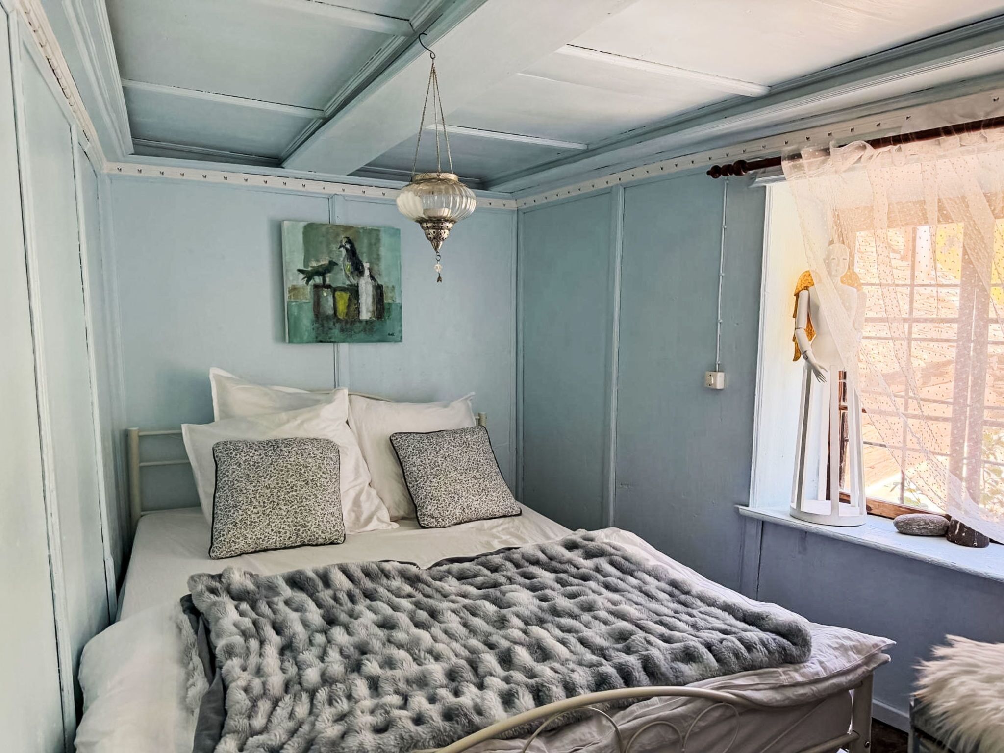 A bedroom with a bed, a painting, a chandelier, and a window with curtains.