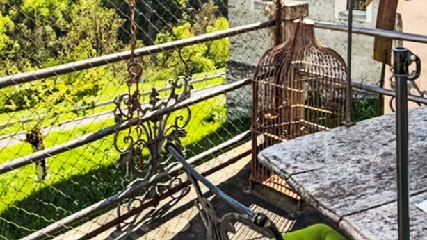 En balkon med udsigt over et bjerglandskab, en fuglebur og en rustik bygning.