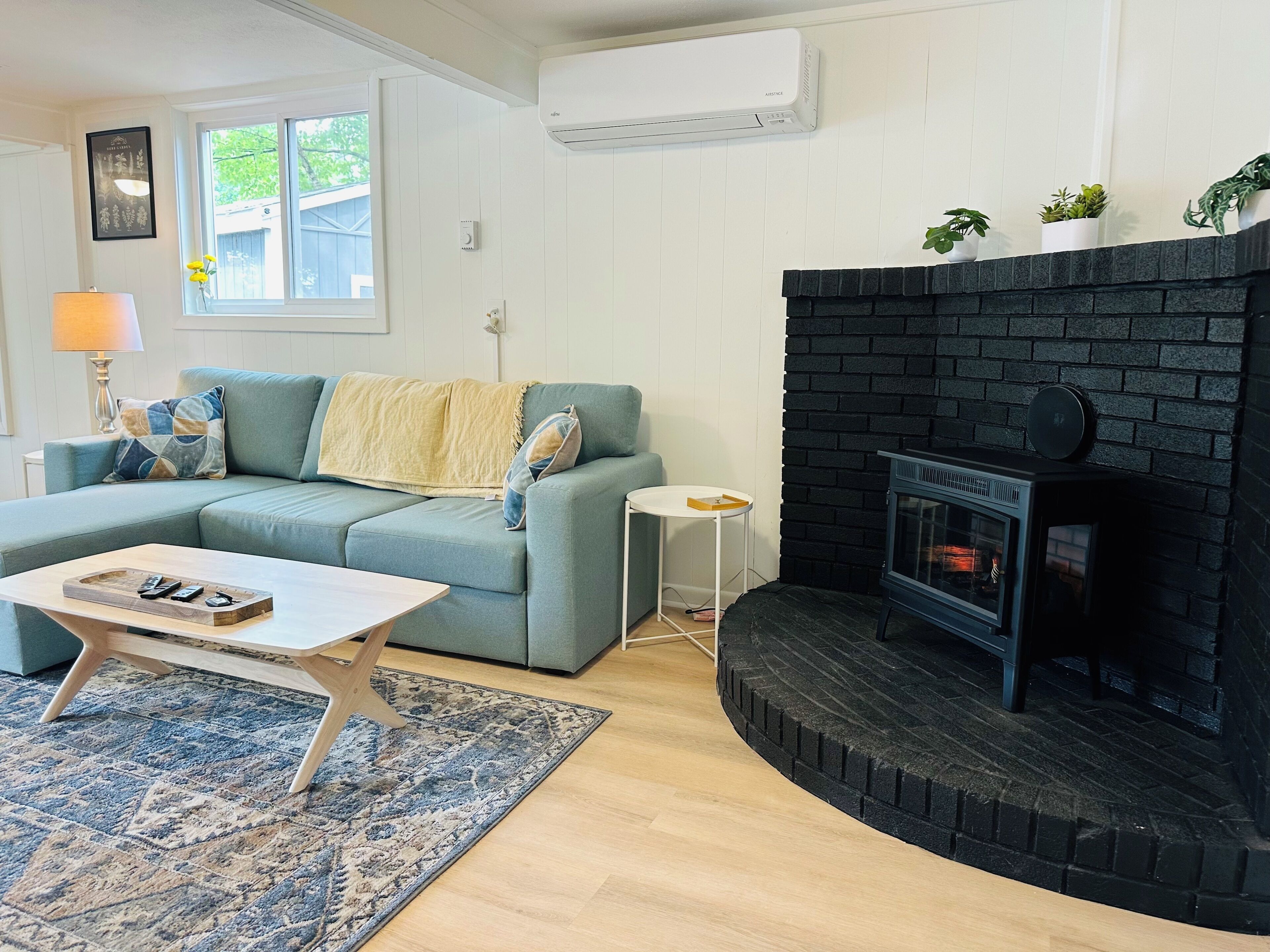 Una sala de estar con un sofá azul, una mesa de centro, una chimenea y una ventana con vistas a zonas verdes.