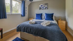 Makuuhuone, jossa on sänky, kaksi yöpöytää, ikkuna, jossa on verhot, seinään kiinnitetty valaisin ja taulu.