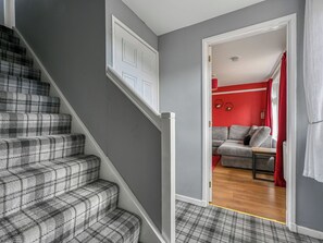 A staircase with a checkered carpet, a grey wall, and a red room with a sofa and curtains. - Cannich Cottage by Interhome (Cannich)