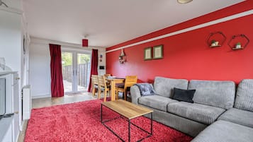 Ein Wohnzimmer mit rotem Teppich, einem grauen Sofa, einem Holztisch und einem Essbereich mit Holztisch und Stühlen.
