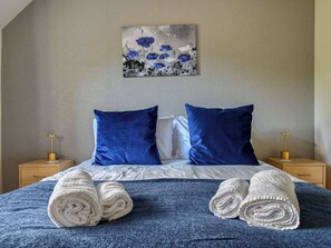 Una cama bien hecha con ropa de cama azul y blanca, dos almohadas y toallas enrolladas sobre la cama.