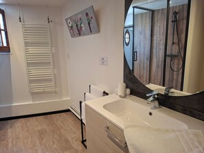 Ein modernes Badezimmer mit einem großen Waschbecken, einem Spiegel, einer Dusche und einem Fenster mit Jalousien.