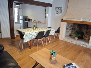 Ein Essbereich mit Tisch für vier Personen, Kamin und einer Küche im Hintergrund.