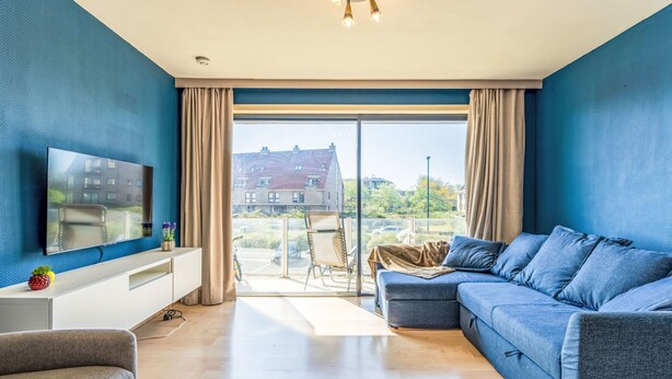 En moderne stue med stort fjernsyn, sofa, lænestol og spiseplads med bord og stole.