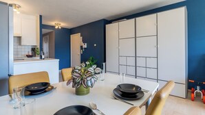 Spiseområde med et bord dækket til to, et køkken i baggrunden og et skydelågeskab.