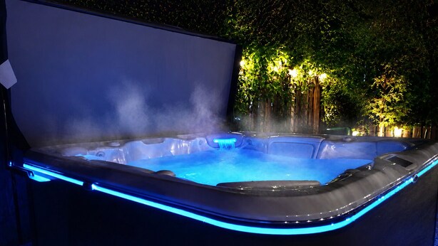A hot tub with blue LED lighting, surrounded by trees and a wooden fence.