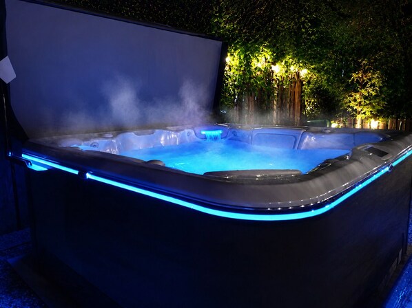A hot tub with blue LED lighting, surrounded by trees and a wooden fence.