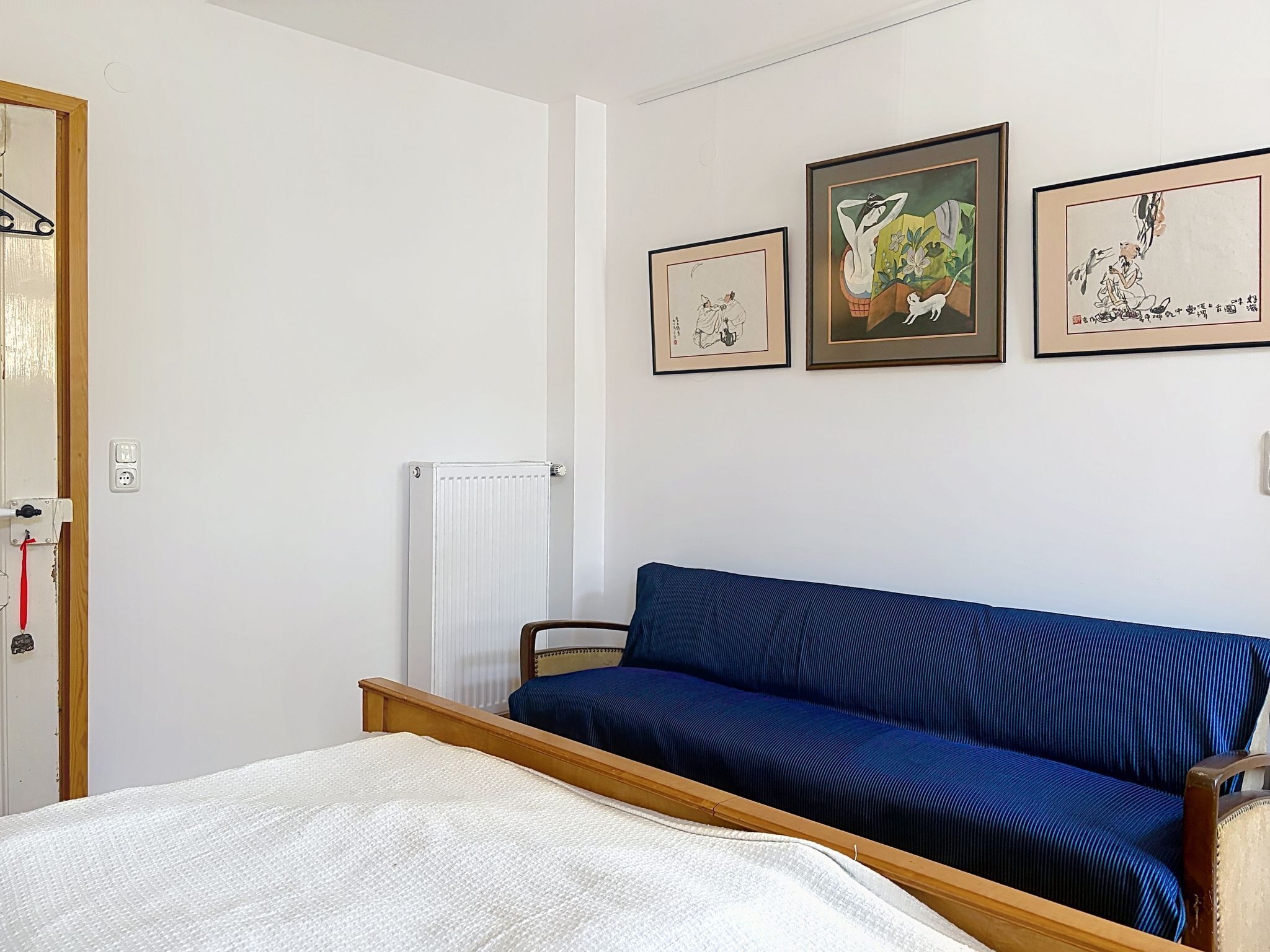A bedroom with a bed, a blue sofa, and three framed artworks on the wall.